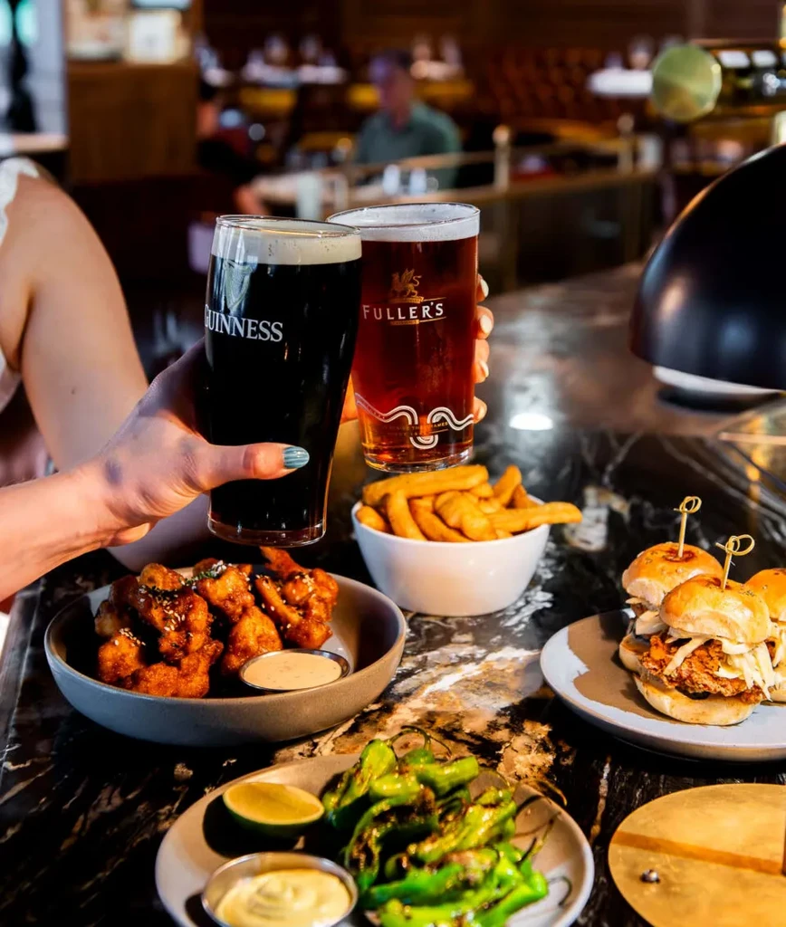 Two beers toasted over fried chicken, fries, peppers, and sliders.