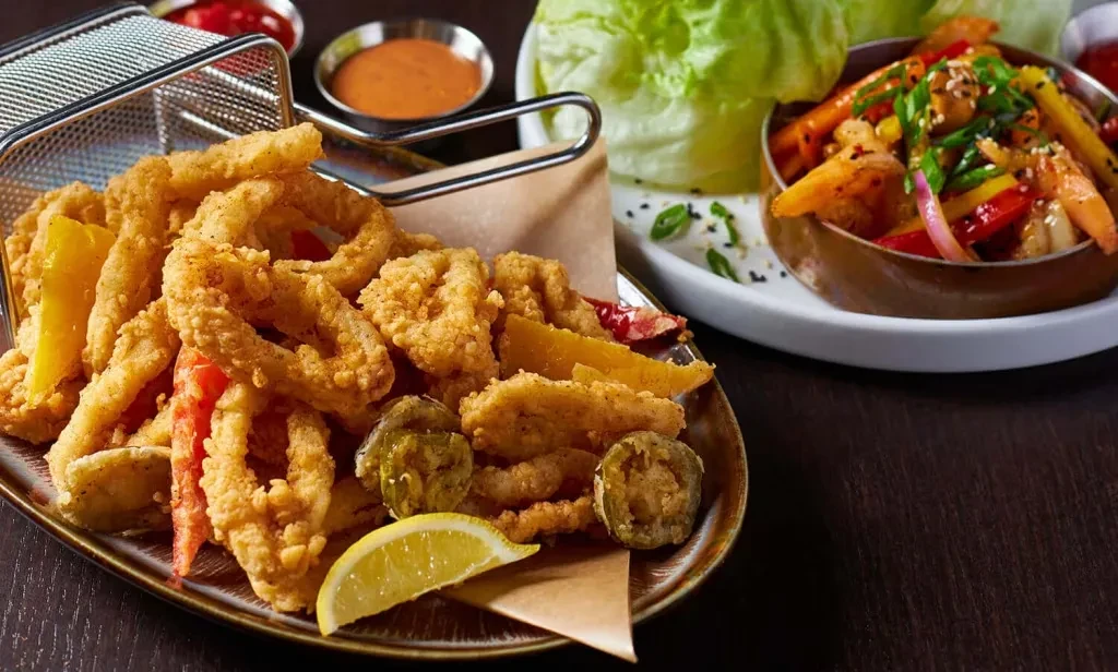 Fried calamari and peppers in a basket, with sauces and other dishes.