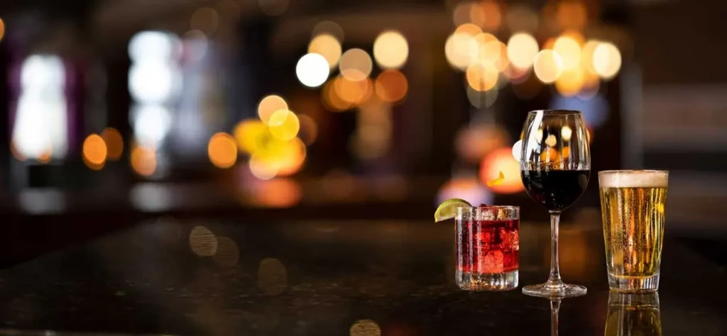 Red cocktail, red wine, and beer on a dark reflective surface.