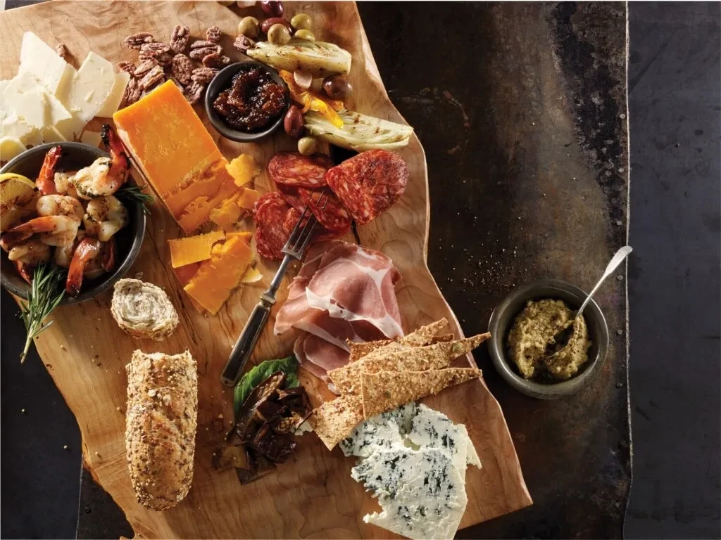 Rustic charcuterie board with cheeses, meats, shrimp, baguette, and spreads.