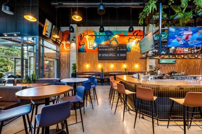 Modern industrial-chic restaurant with diverse seating and baseball on TV.