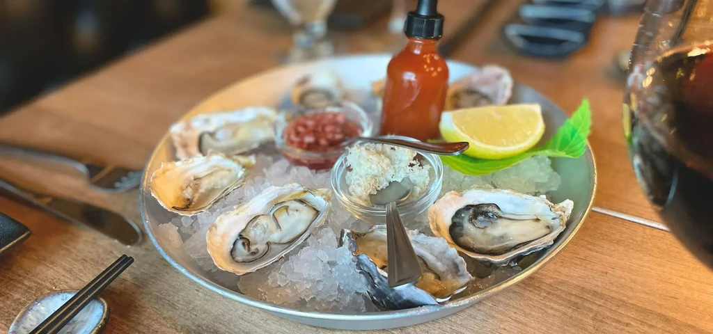 Fresh oysters on crushed ice with condiments, lemon, and chopsticks.