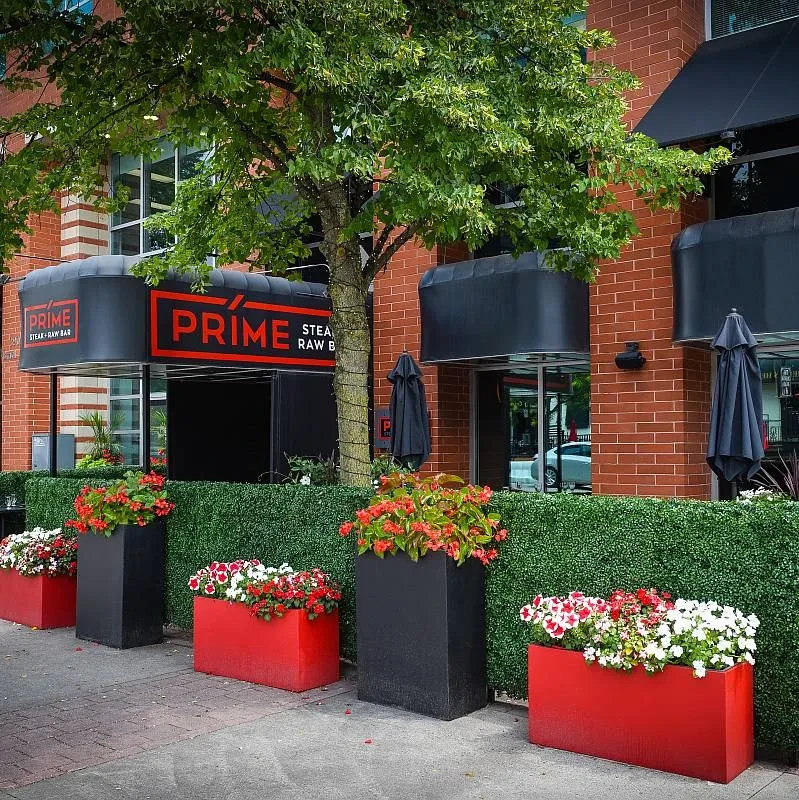 PRIME Steak + Raw Bar restaurant facade with vibrant flowers and lit tree.