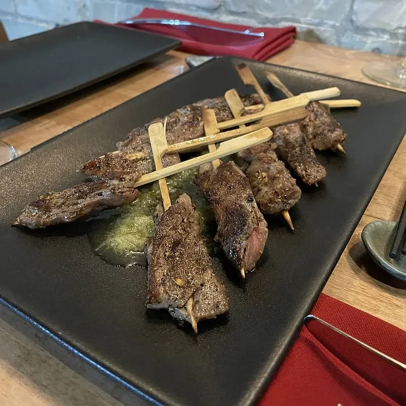 Close-up of grilled meat skewers with green sauce on a black plate.