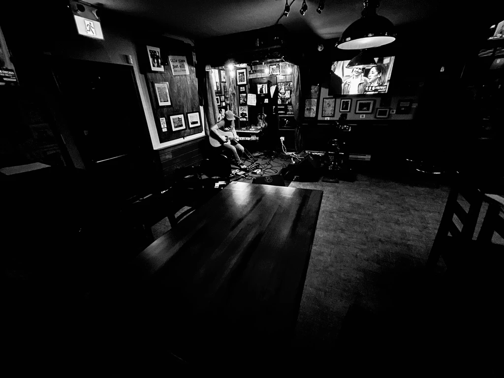 Black and white photo: Musician plays guitar on a dimly lit stage.