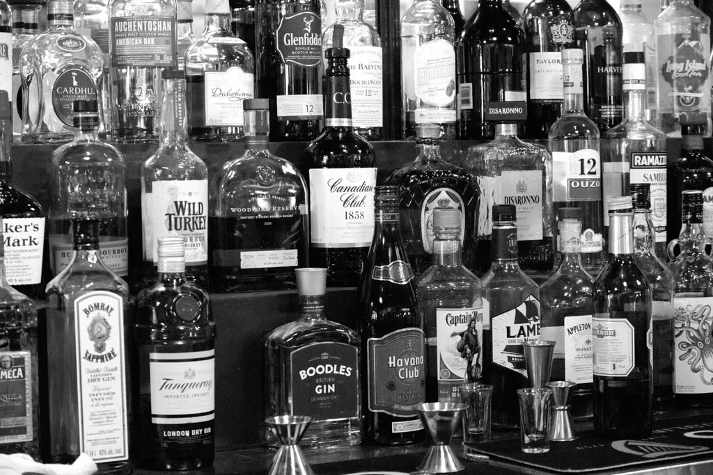 Black and white bar shelf stocked with liquor bottles and bar tools.