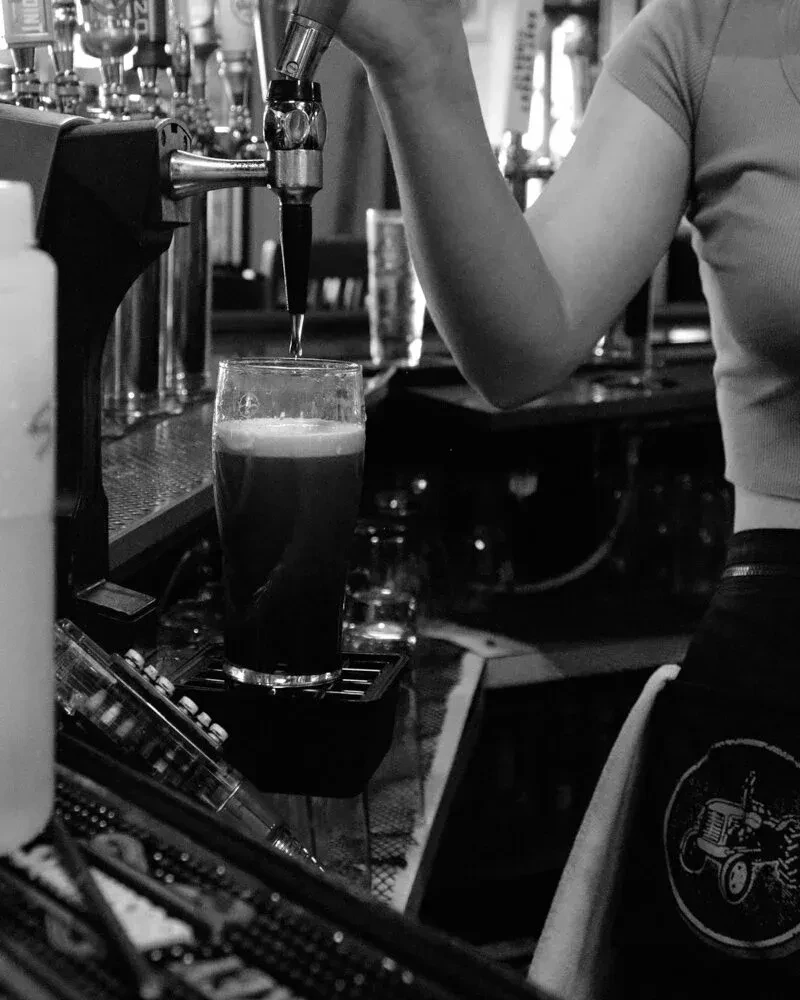 Black and white photo: Bartender's arm pours dark beer from tap.