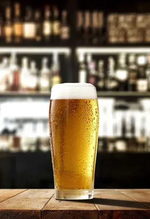 Cold pint of golden beer with foam on rustic wooden table.