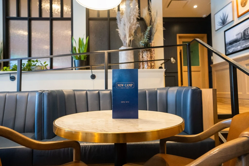 Restaurant interior with round marble table, "NEW CAMP" menu, and navy booth.