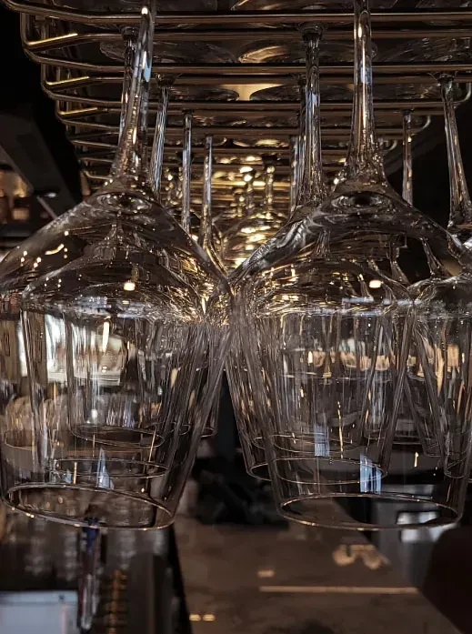 Clear wine and cocktail glasses hanging upside down on a metallic rack.