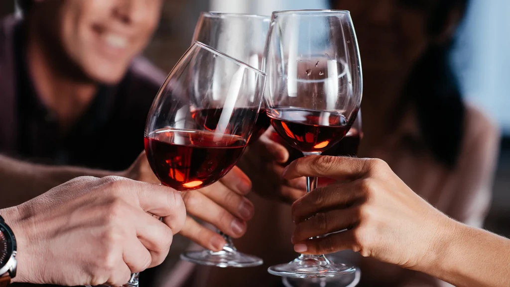Three red wine glasses clink together in a warm toast.