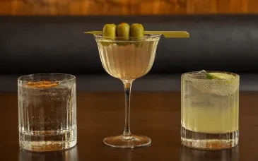 Three distinct cocktails in various glasses on a dark wooden surface.