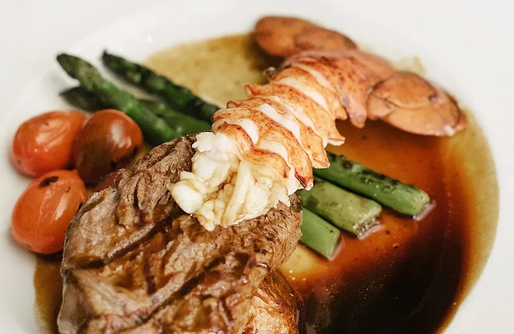 Plated surf and turf: medium-rare steak, lobster, asparagus, and tomatoes.