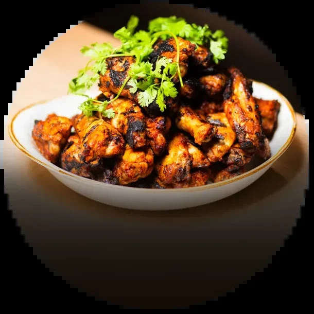 Charred, glossy grilled chicken pieces in a bowl with cilantro.