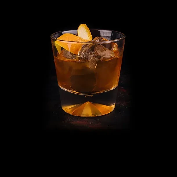 Amber cocktail with ice and orange peels in a rocks glass.