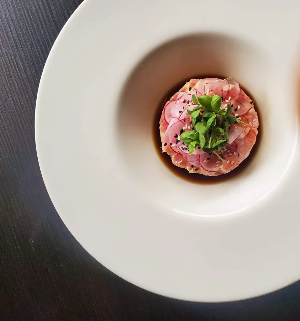 Plated raw fish tartare with radishes, microgreens, sesame seeds in white bowl.