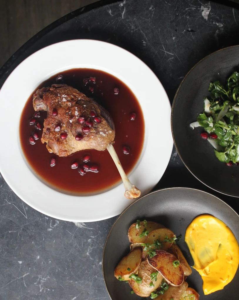 Overhead: Crispy duck leg, salad, potatoes, yellow sauce on stone table.