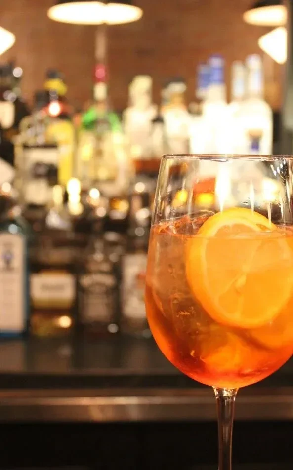 Orange cocktail with ice and citrus slice, blurred bar background.