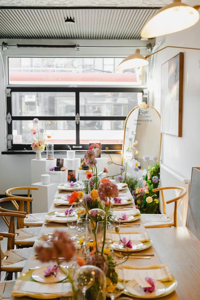 Modern dining table with settings, colorful flowers, and a Saje display.
