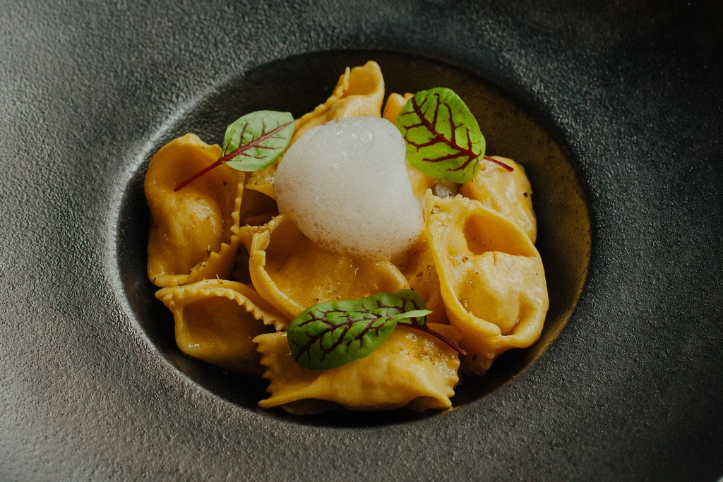 Close-up of golden tortellini-like pasta with white foam and green garnish.