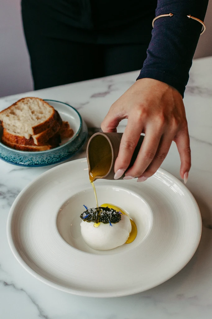 Hand pours oil over burrata topped with caviar and flowers.