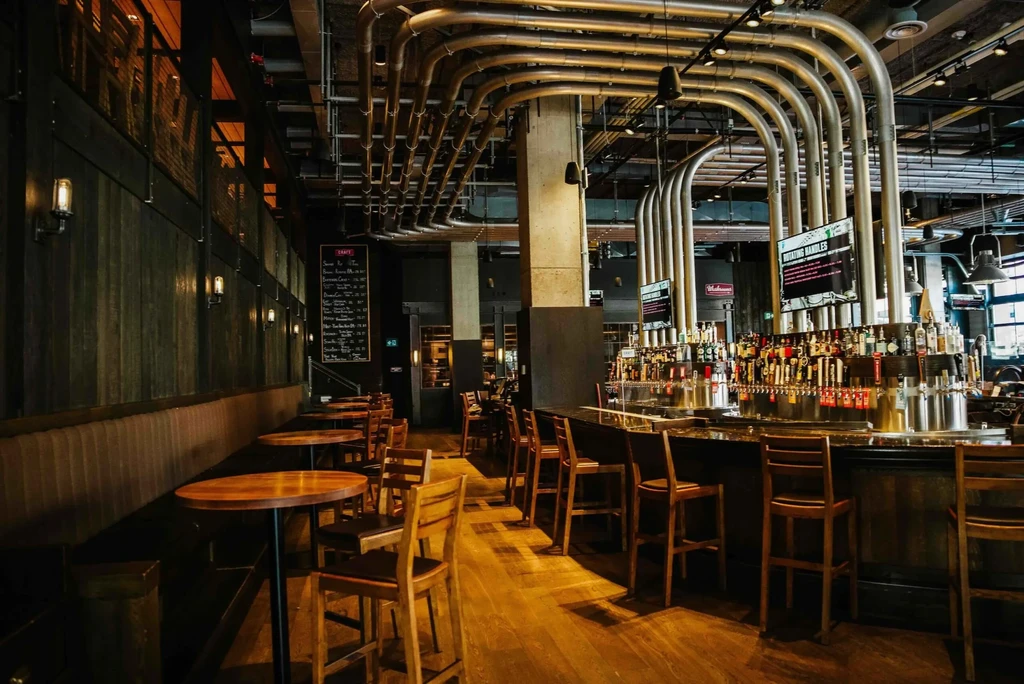 Industrial-chic bar with beer taps, exposed pipes, and seating.