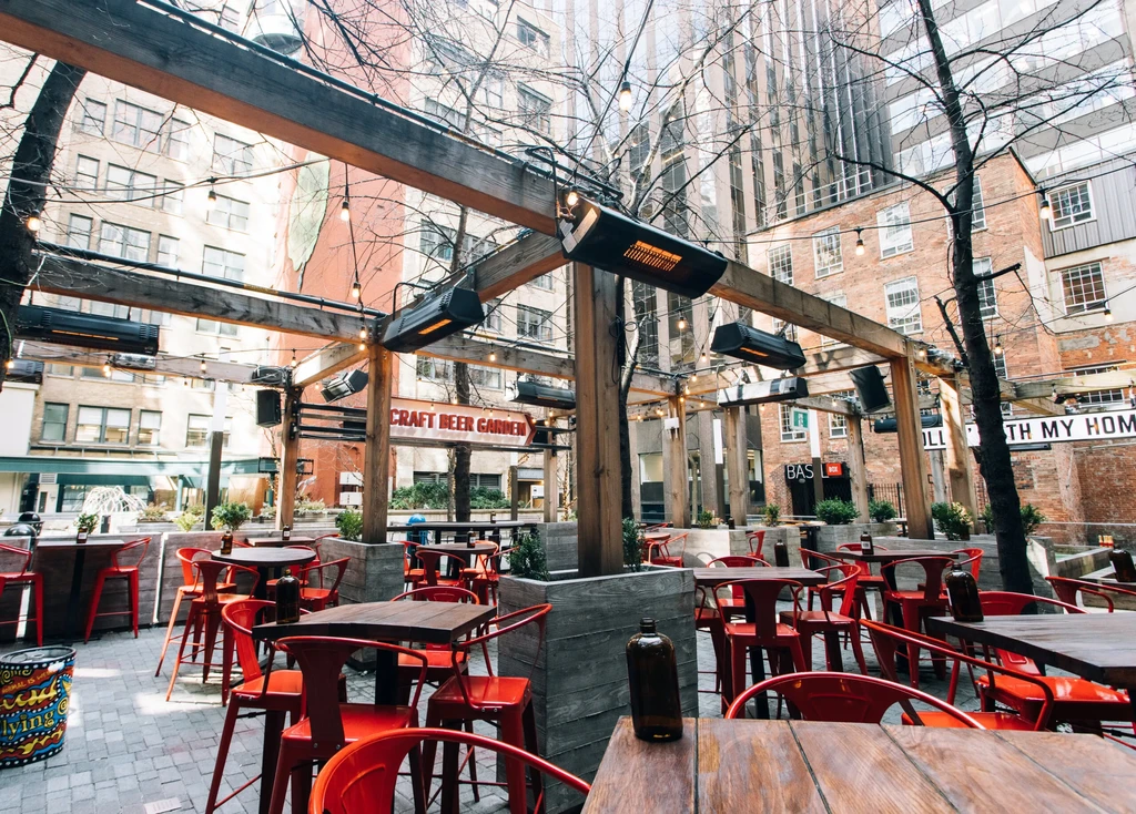 Empty urban craft beer garden with red chairs under a lighted pergola.