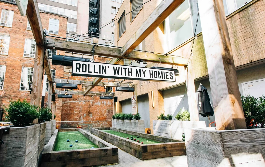 Two outdoor bocce ball courts with turf and "ROLLIN' WITH MY HOMIES" sign.
