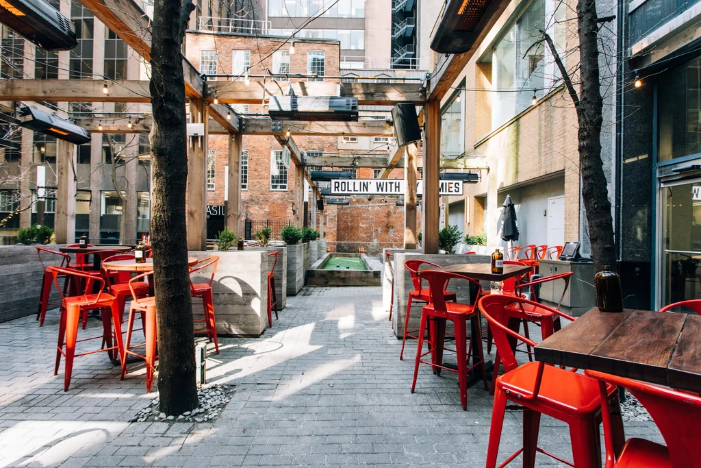 Outdoor patio with red chairs, wooden pergola, heaters, and urban background.