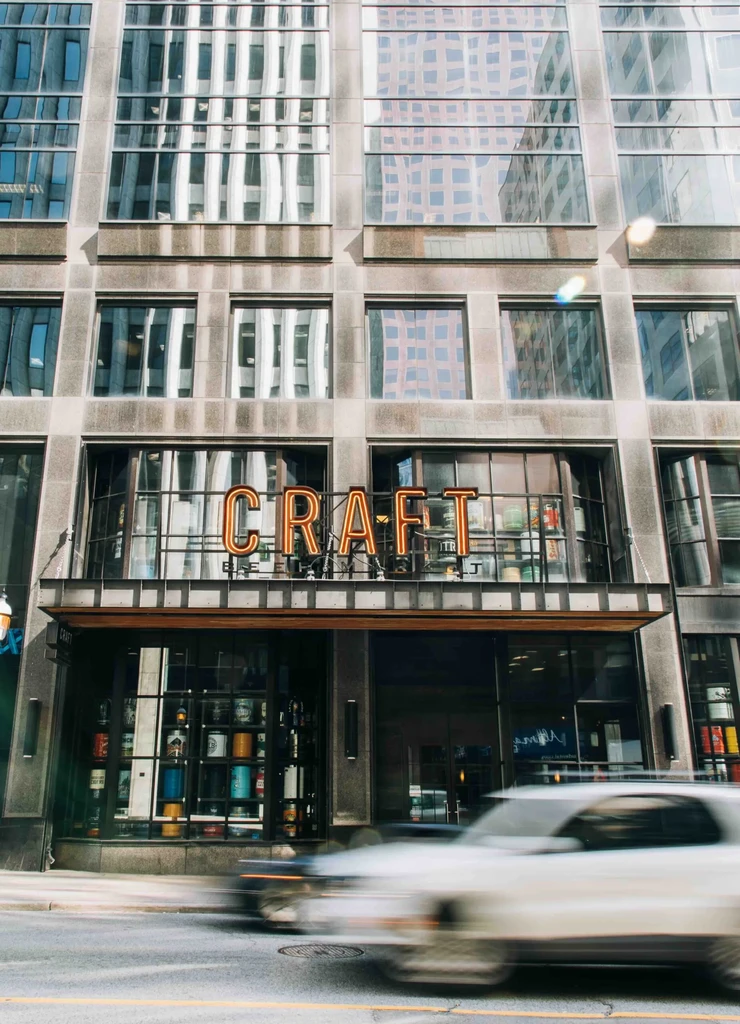 Orange neon 'CRAFT' sign on a modern city building storefront.