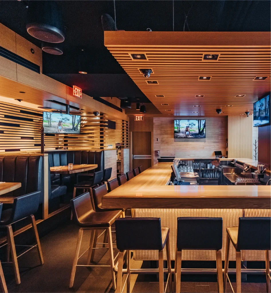 Modern bar and dining area with warm wood, dark seating, TVs.