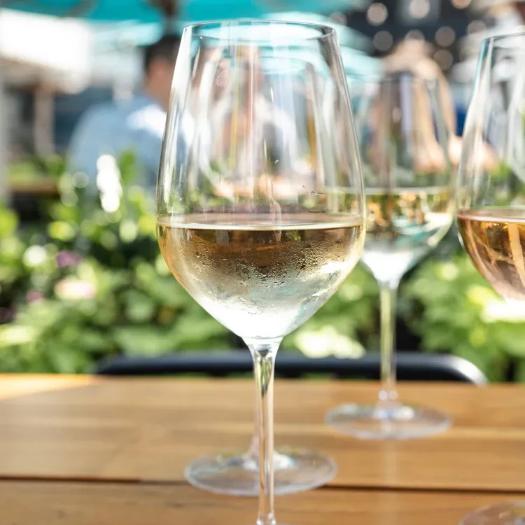 A condensing wine glass on a wooden table with blurred outdoor background.