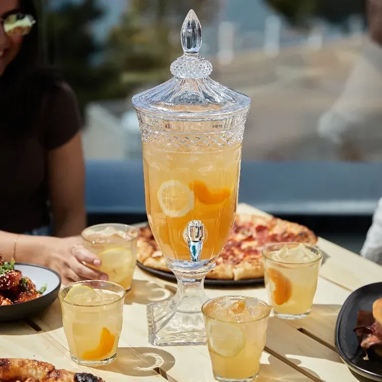 Outdoor dining scene with beverage dispenser, food, and people.