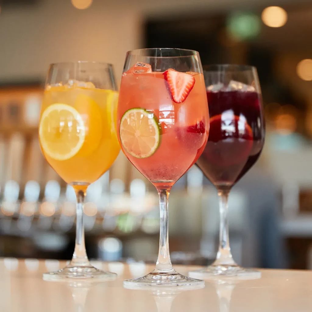 Three colorful cocktails with garnishes on a reflective bar top.