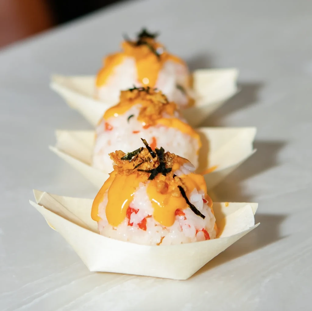 Three rice balls topped with yellow sauce, nori, and crispy bits.