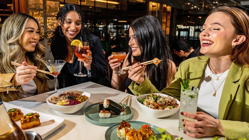 Four young women laughing over dinner and cocktails at a restaurant.