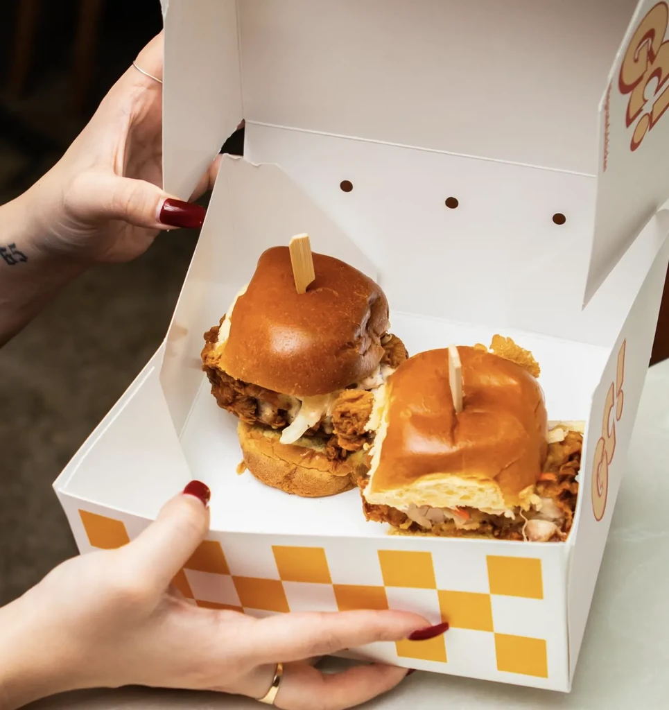 Two fried chicken sandwiches on brioche buns in an open takeout box.