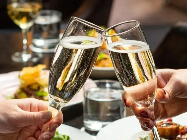 Two champagne flutes clink together in a restaurant toast.
