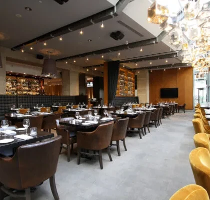 Modern, empty restaurant interior featuring set tables, bar, and geometric lights.