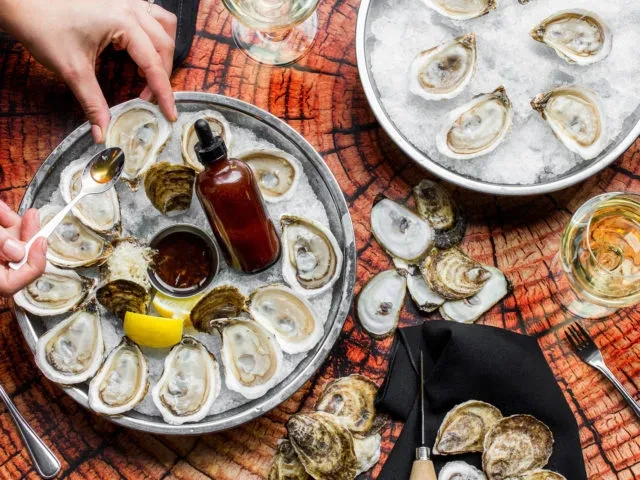 Overhead shot of a lavish oyster spread with hands and wine.