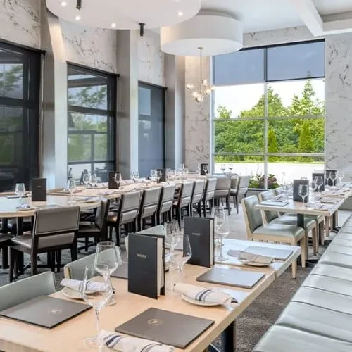 Modern, elegant restaurant dining room with set tables and outdoor greenery.