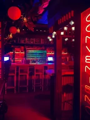 Dimly lit bar interior, empty, illuminated by red and blue neon.