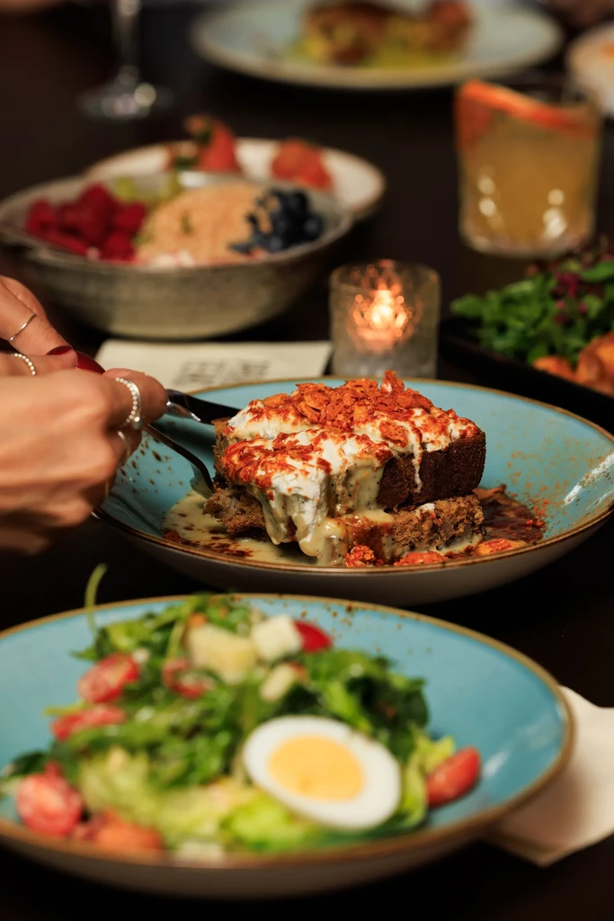 Hands cutting savory dish with white sauce and crispy garnish.