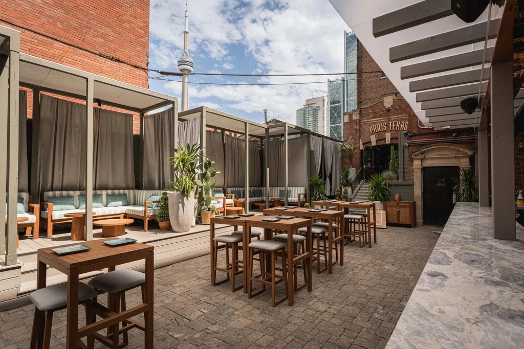 Urban restaurant patio with cabanas, tables, and Toronto CN Tower.