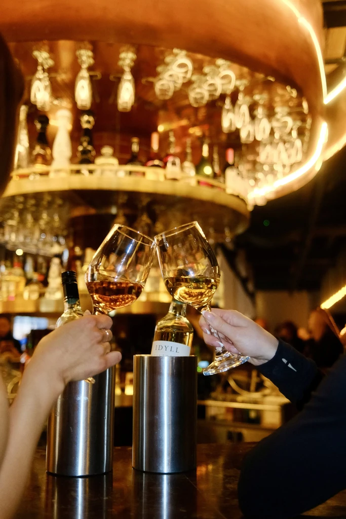 Hands clinking wine glasses together in a warm, upscale bar.