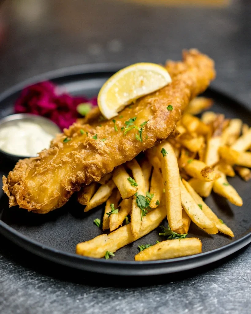 Close-up of a plate with golden battered fish, fries, sauce, and cabbage.
