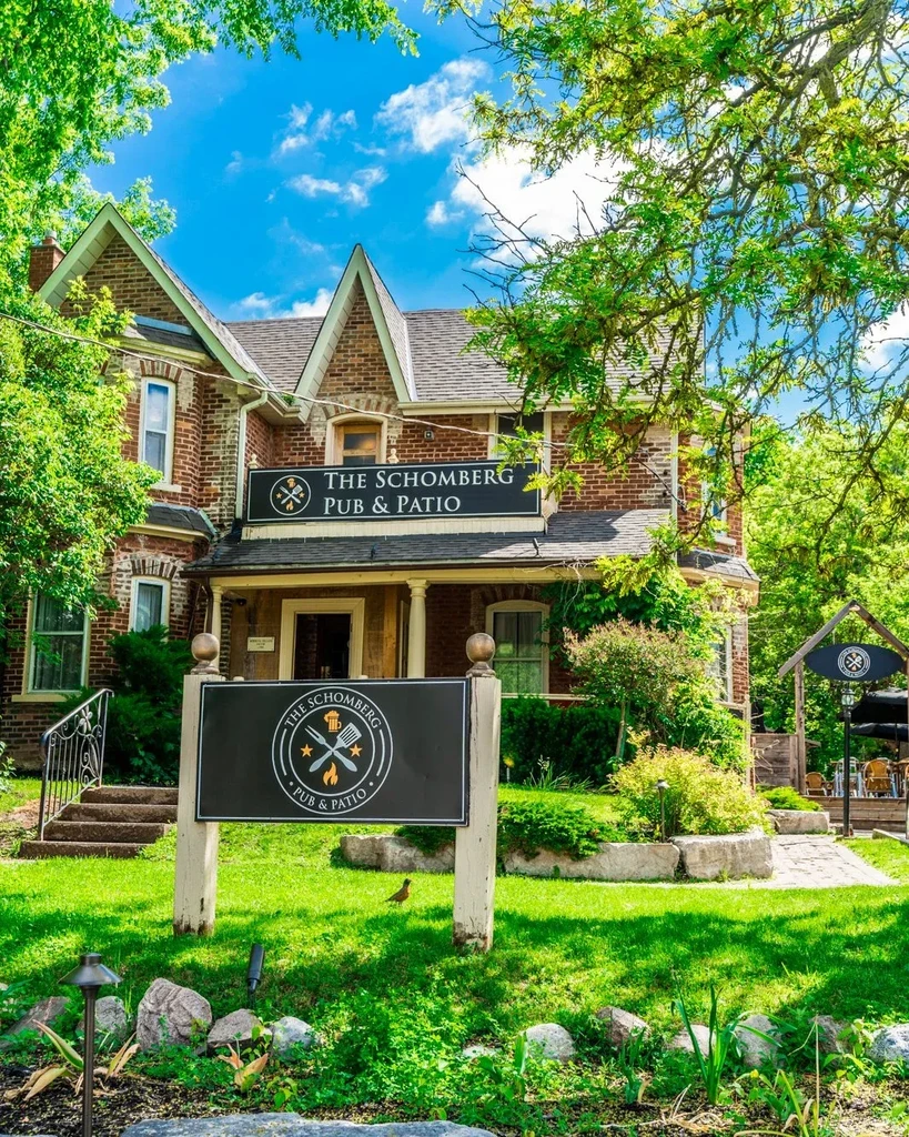 The Schomberg Pub & Patio: brick building, signs, and lush outdoor dining.