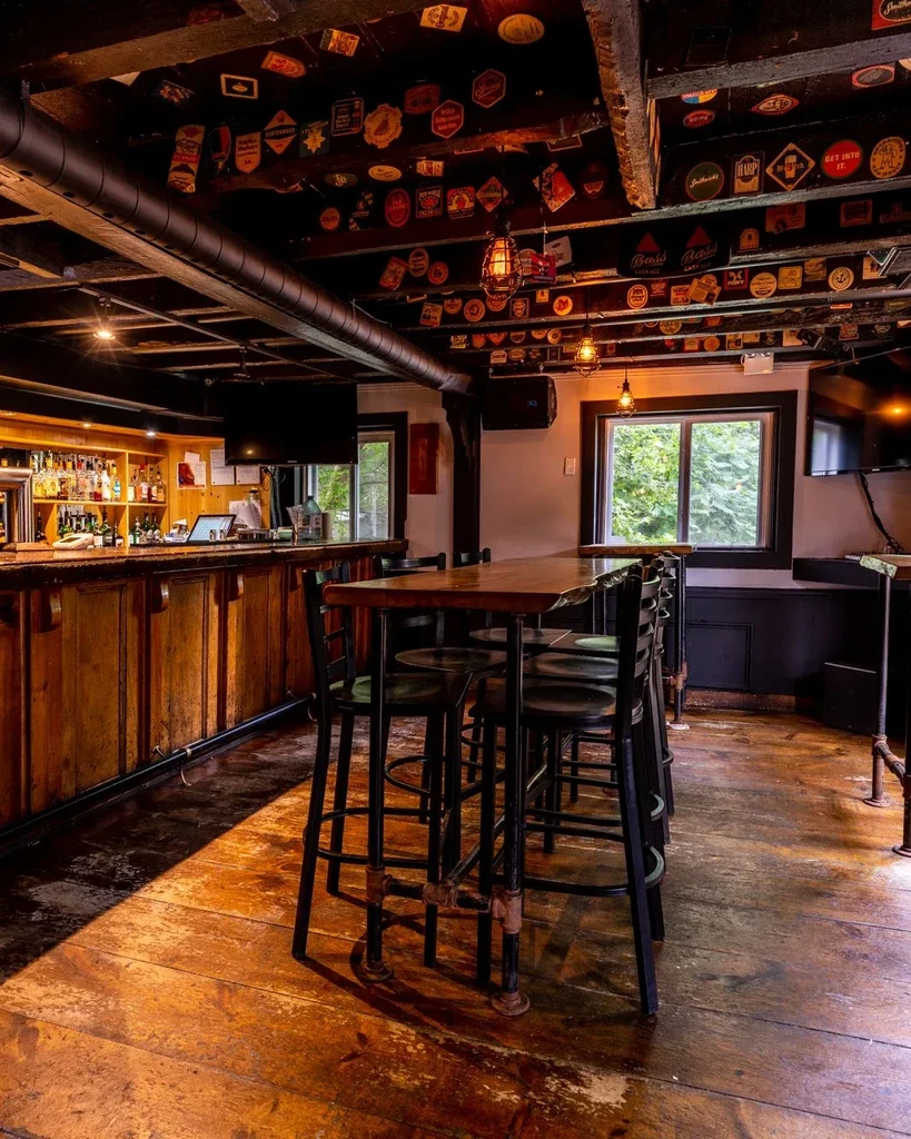 Rustic bar with wooden bar, high table, and unique coaster-decorated ceiling.