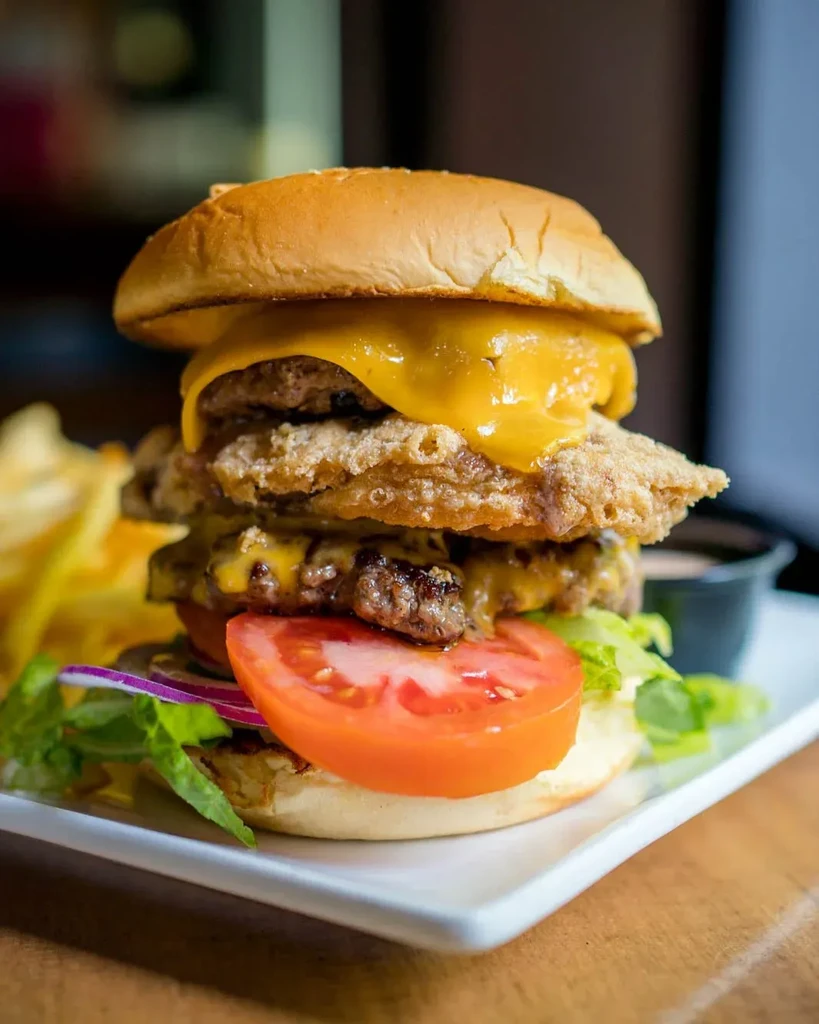Close-up of a multi-layered chicken and beef burger with cheese and vegetables.