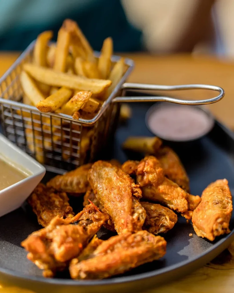Golden chicken wings, french fries, and two sauces on a dark plate.